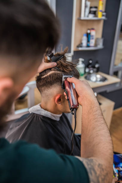 Barber cutting hair to his young customer with his trimmer