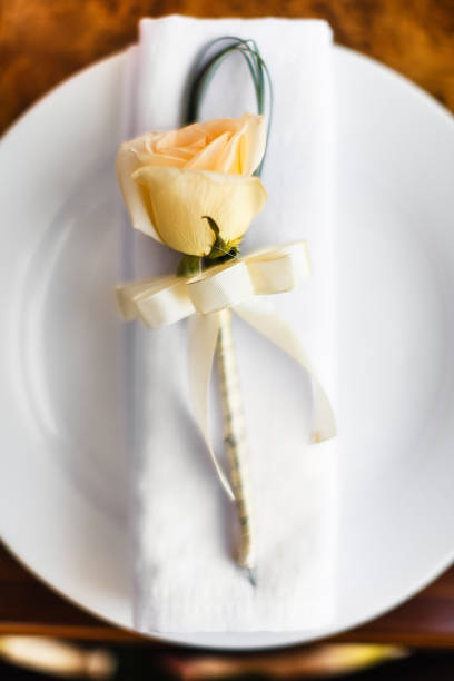 Place setting in soft focus, with delicate peach flower.  shallow depth of field.  More place settings and cutlery: