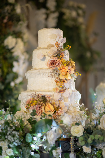 A beautiful wedding cake on a round table surrounded with fresh flowers. 