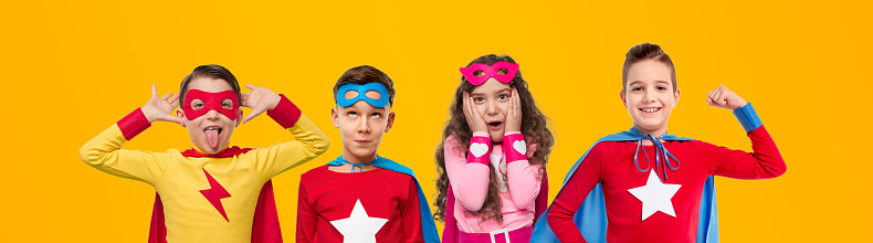 Collage of cute kids in bright superhero costumers gesticulating and grimacing against yellow background