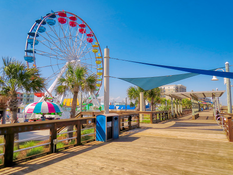 A colorful ocean boardwalk scene at Carolina Beach with a large Ferris wheel under a sunny blue sky.
