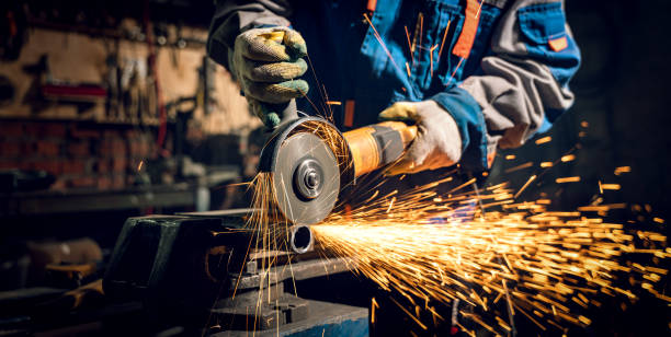 Locksmith in special clothes and goggles works in production. Metal processing with angle grinder. Sparks in metalworking Locksmith in special clothes and goggles works in production. Metal processing with angle grinder. Sparks in metalworking. steel grinding stock pictures, royalty-free photos & images