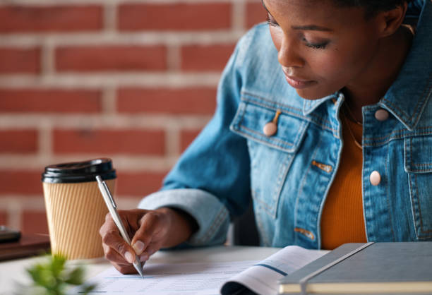 una joven enfocada firmando documentos financieros para su seguro de hogar. una joven firmando una solicitud de préstamo en el banco para pagar sus cuentas. una mujer leyendo y firmando documentos para una inversión - success signing businesswoman serious fotografías e imágenes de stock