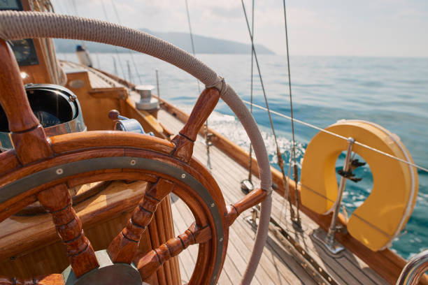 nahaufnahme des holzlenkrads auf einem leeren boot, das den ozean befährt. nahaufnahme des leeren bootsdecks mit rigging-kabeln holzlenkrad, das den ozean befährt. - rope rigging nautical vessel day stock-fotos und bilder