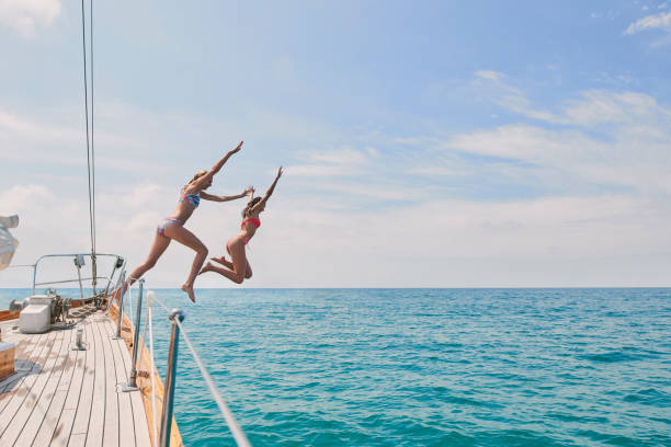 Carefree excited young women jumping from boat to swim in the ocean. Two friends on a holiday cruise together jumping from boat into the ocean to swim. Excited young women jumping off boat together Carefree excited young women jumping from boat to swim in the ocean. Two friends on a holiday cruise together jumping from boat into the ocean to swim. Excited young women jumping off boat together diving into water stock pictures, royalty-free photos & images