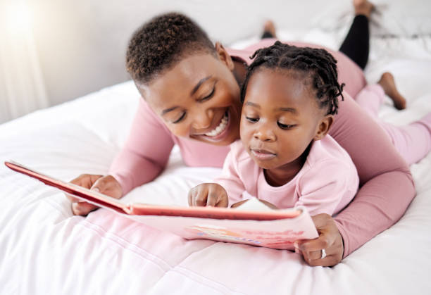 shot of a beautiful young woman bonding with her daughter in bed at home - family reading african descent book imagens e fotografias de stock