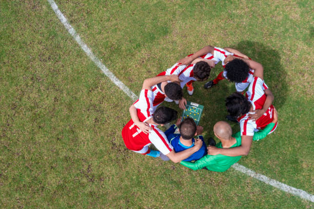 trainer spricht mit einer mannschaft von fußballspielern über ihre strategie für das spiel - köpfe zusammenstecken stock-fotos und bilder