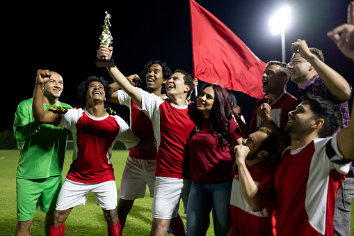 Soccer team celebrating their victory with a group of fans in the field and lifting the trophy - winning concepts