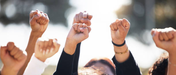 shot of a group of people protesting together in solidarity - women standing fist success imagens e fotografias de stock