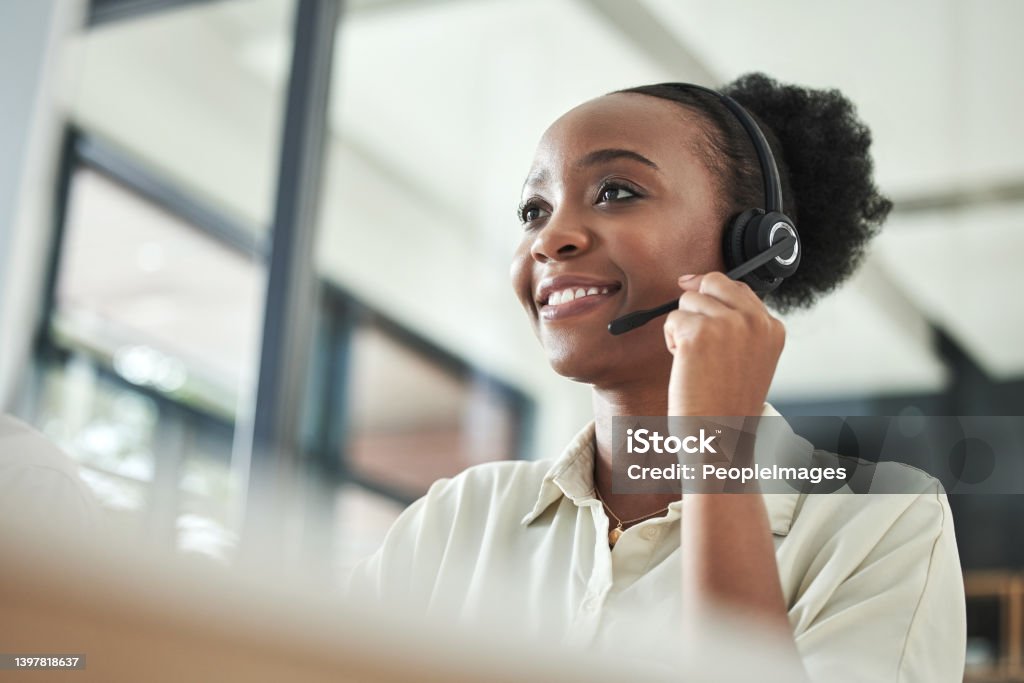Low angle shot of an attractive young call centre agent sitting alone in the office and using her computer How may I help? Customer Service Representative Stock Photo