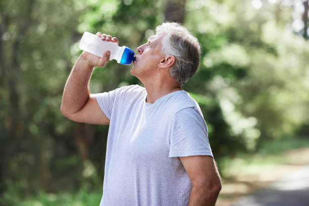 scatto di un uomo maturo che beve acqua mentre si esercita all'aperto - drinking men water bottle foto e immagini stock