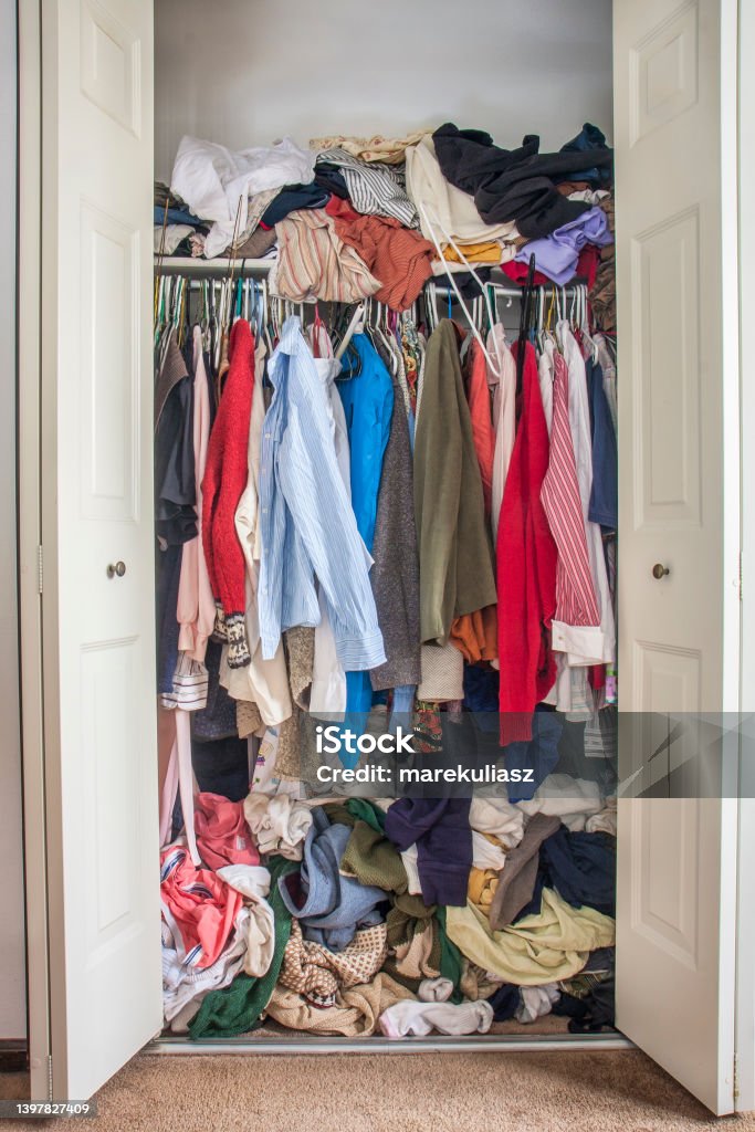 messy closet overfilled with clothes messy closet overfilled with colorful woman clothes on hangers and stuffed in any available space, need for declutter concept Decluttering Stock Photo