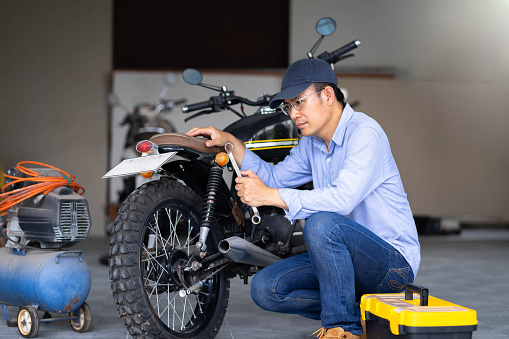Portrait of man mechanic in garage or workshop inspecting classic motorcycle during the maintenance.