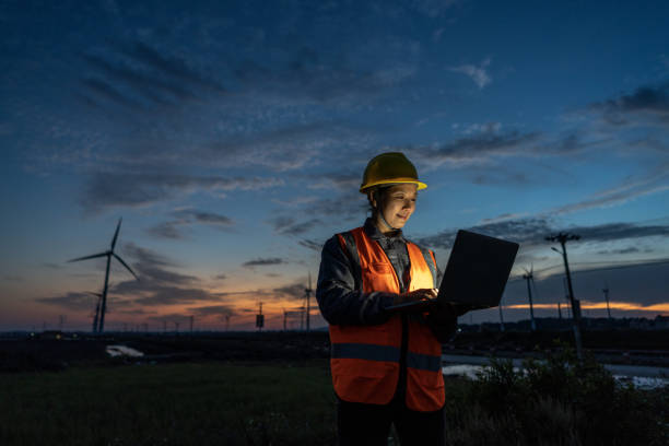 an asian female wind power engineer on the night shift works with a computer under the wind turbine - power supply power supply box power equipment imagens e fotografias de stock