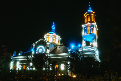 Color image depicting the exterior architecture of an orthodox church in the Transylvania region of Romania. It is night and the church is beautifully illuminated with blue and gold light.