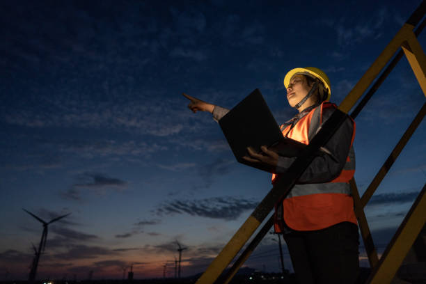 istock A female engineer on the night shift works with a computer and points to the wind turbine in the distance 1397829568