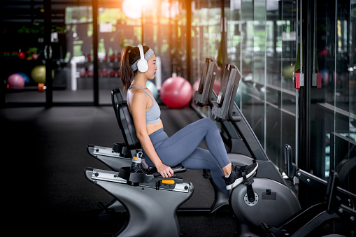 Fitness woman wearing sportwear and workout headband on  in the gym. Woman is setting setup machine stationary bike screen options at gym.