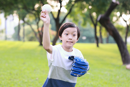 A smiling eight years old girl is about to throw a baseball. She is wearing a blue shirt and a pink short. She is playing a baseball game with her family in a park in Quebec, Canada. We can see her dad behind her at the second base.
