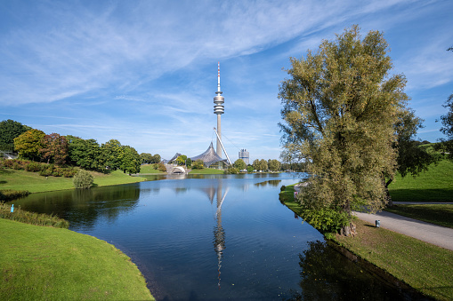 Munich, Germany - October 11, 2021:  Olympia Tower in Munich reflecting in lake in Olympiapark under blue sky