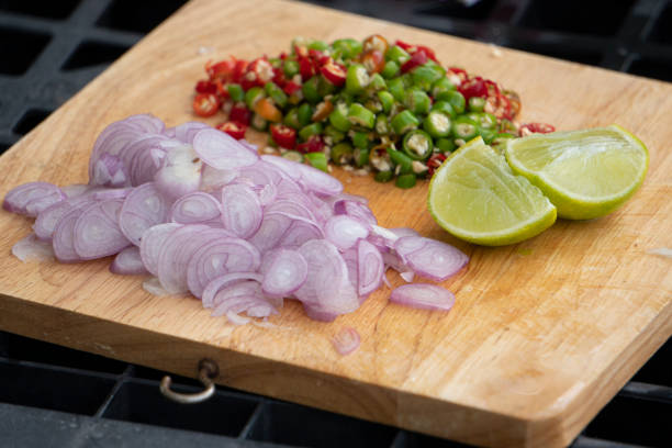 Side dishes of Red onion, fresh chili, lime are sliced on a wooden chopping board. stock photo