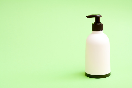 White plastic soap bottle with blat top and bottom on green background with free copy paste space for text.
