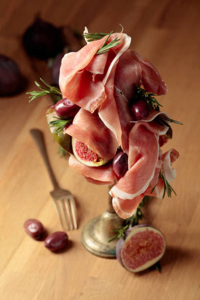 Prosciutto with figs, rosemary, and red olives on a old wooden table.