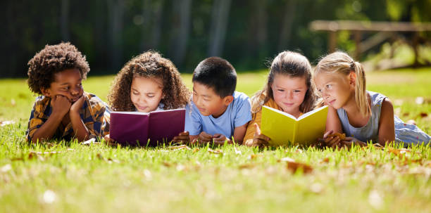 aufnahme einer gruppe von kindern, die draußen ein buch lesen - lesen stock-fotos und bilder
