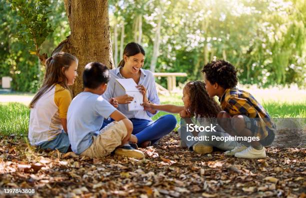 Shot Of A Teacher Reading A Book To Her Class In A Park Stock Photo - Download Image Now