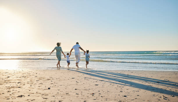 rearview shot of a happy family walking towards the sea - beach stockfoto's en -beelden
