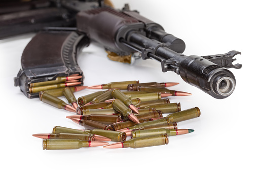 Heap of the service rifle cartridges on a blurred background of the front end of the assault rifle and loaded rifle magazine on a white background, selective focus