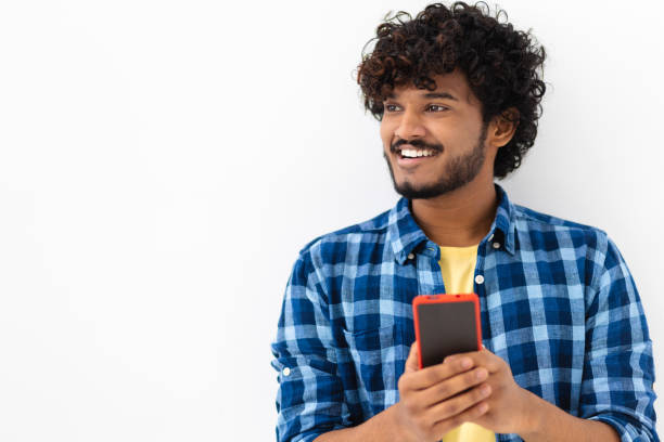 istock Young joyful Asian man using mobile phone looking away and smiling standing on a white background. Chatting online or playing games concept 1397844947