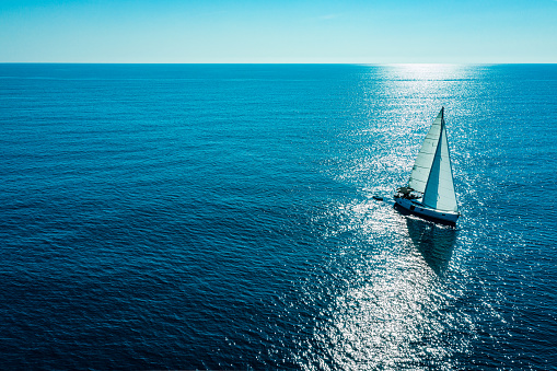 The calm water. White sloop rigged yacht sailing at sunset. A view from the deck to the bow, mast and the sails. Baltic Sea, Latvia