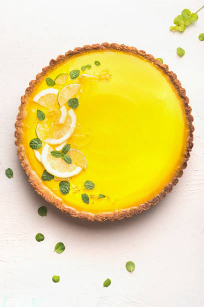 Lemon tart topped with citrus slices and zest on white table background, top view. stock photo