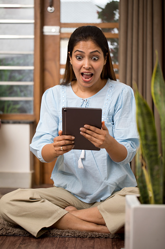 Surprised young woman using digital tablet at home