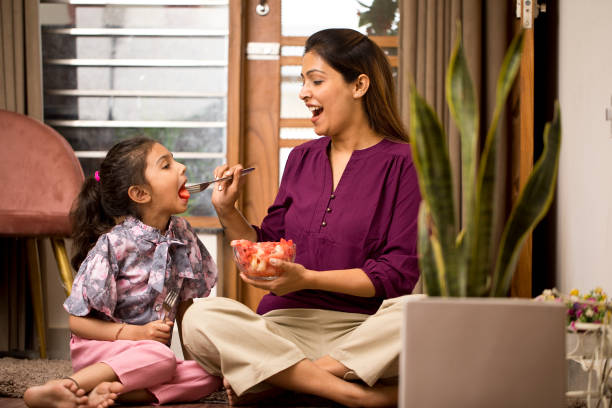 Happy mother feeding fruit to daughter at home stock photo