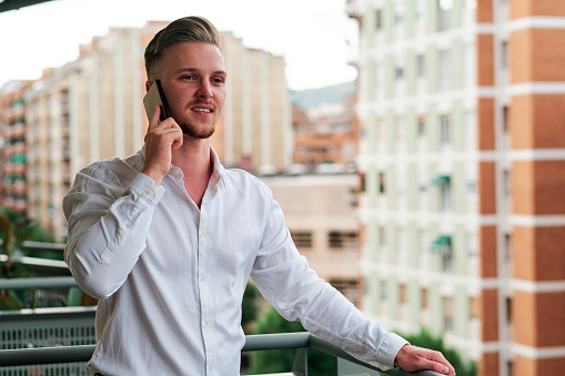 Young executive businessman talking on the mobile phone while standing on a balcony outdoors. Business and technology concept.