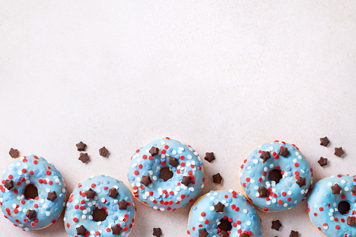 Fresh doughnuts in blue, red and white colors for 4th of July, Independence day in USA. Patriotic holiday food, 4th July donuts border on light gray, copy space