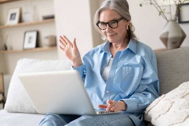 istock Smiling 50s mature woman sitting on sofa, using laptop, working, chatting, spending time in social media 1397857217