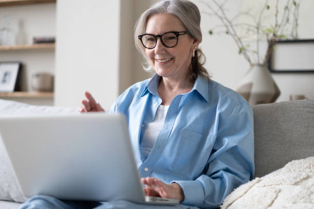 istock Smiling 50s mature woman sitting on sofa, using laptop, working, chatting, spending time in social media 1397857248