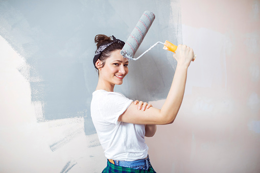 Young cheerful woman have a fun and painting her home
