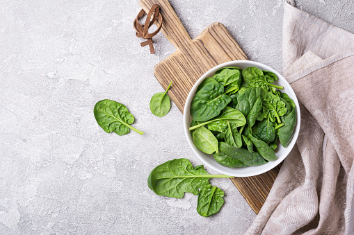 Top view of bowl with green fresh baby spinach on wooden board and grey concrete background