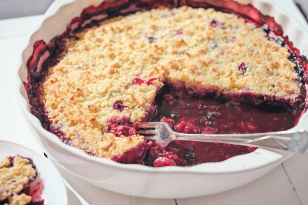 plat de cuisson en céramique blanche avec une tarte aux myrtilles. fourchette laissée sur une tarte. cuisson à la maison, en utilisant des baies de jardin, repas sain. lumière directe du soleil. - pie fruit cobbler sweet food photos et images de collection