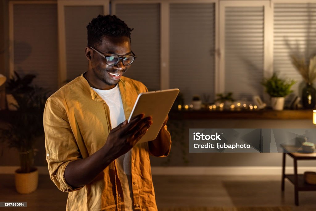 Making days at home so much more entertaining Shot of a handsome young businessman using a digital tablet while working late at home. Digital Tablet Stock Photo