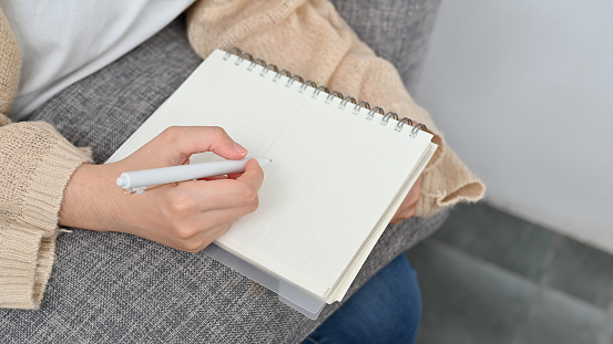 Female taking notes on spiral notepad, hand writing something on blank paper, noting list on notebook or writing a diary. cropped