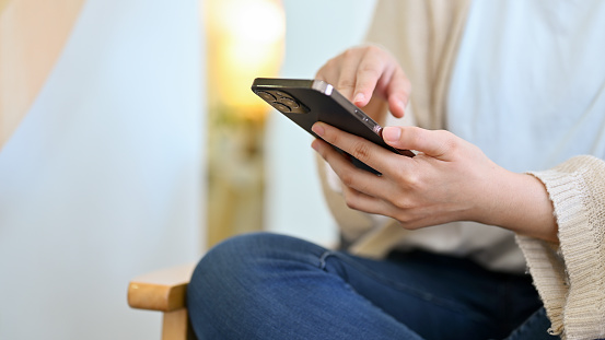 Woman taking a break in her living room, watching online content, using smartphone. cropped, closeup