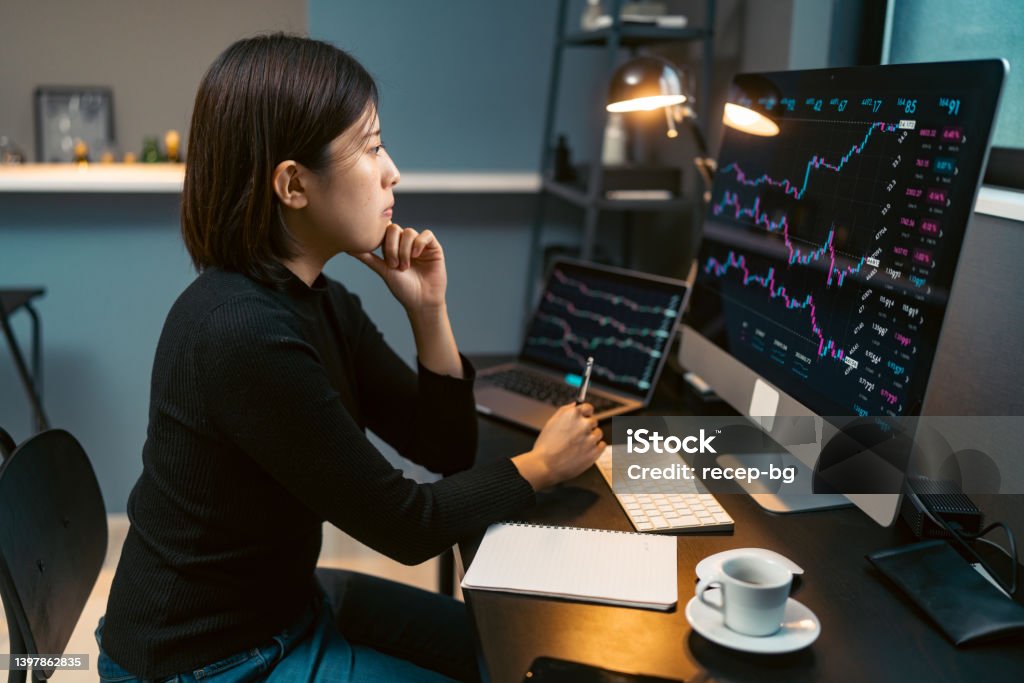 Young woman doing cryptocurrency business trading on her computer at home at nigh A young woman is doing cryptocurrency business trading on her computer at home at nigh. Stock Market and Exchange Stock Photo