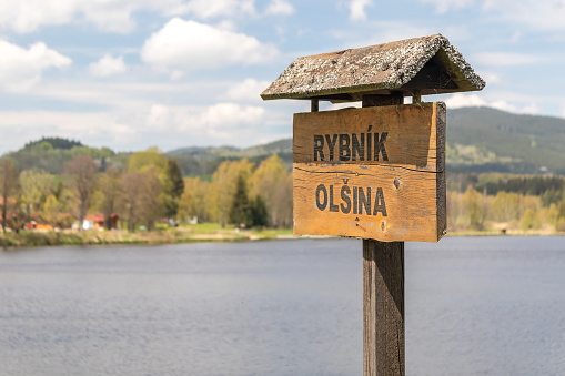 wooden tourist information sign with inscription Olsina Pond, pond in the background