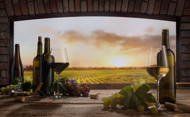 istock Still life with wine glasses, bottles, grapes on wooden table in wine cellar. Panoramic window view of lush vineyards at sunset. 1397864580
