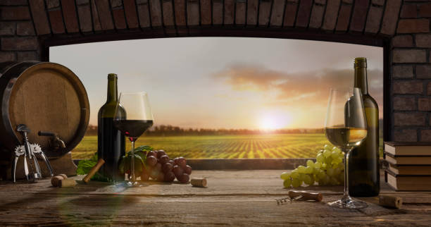 istock Still life with wine glasses, bottles, grapes on wooden table in wine cellar. Panoramic window view of lush vineyards at sunset. 1397864770