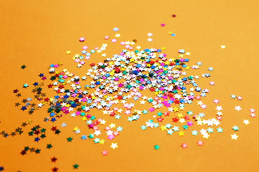 multicolor sparkles on orange background. Festive backdrop for your projects